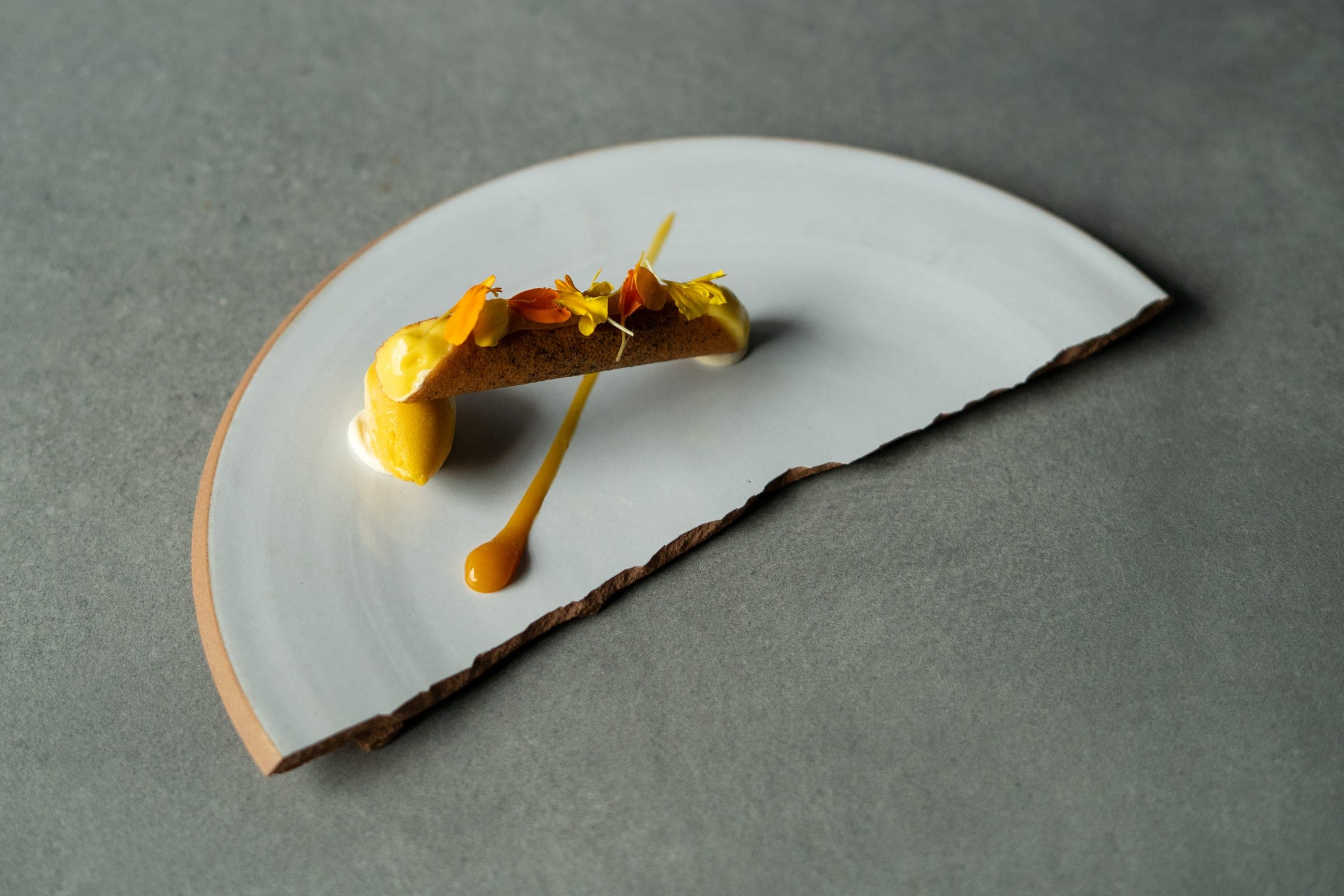 Dessert served on a fan-shaped plate, crisp tuile, sorbet and edible flowers