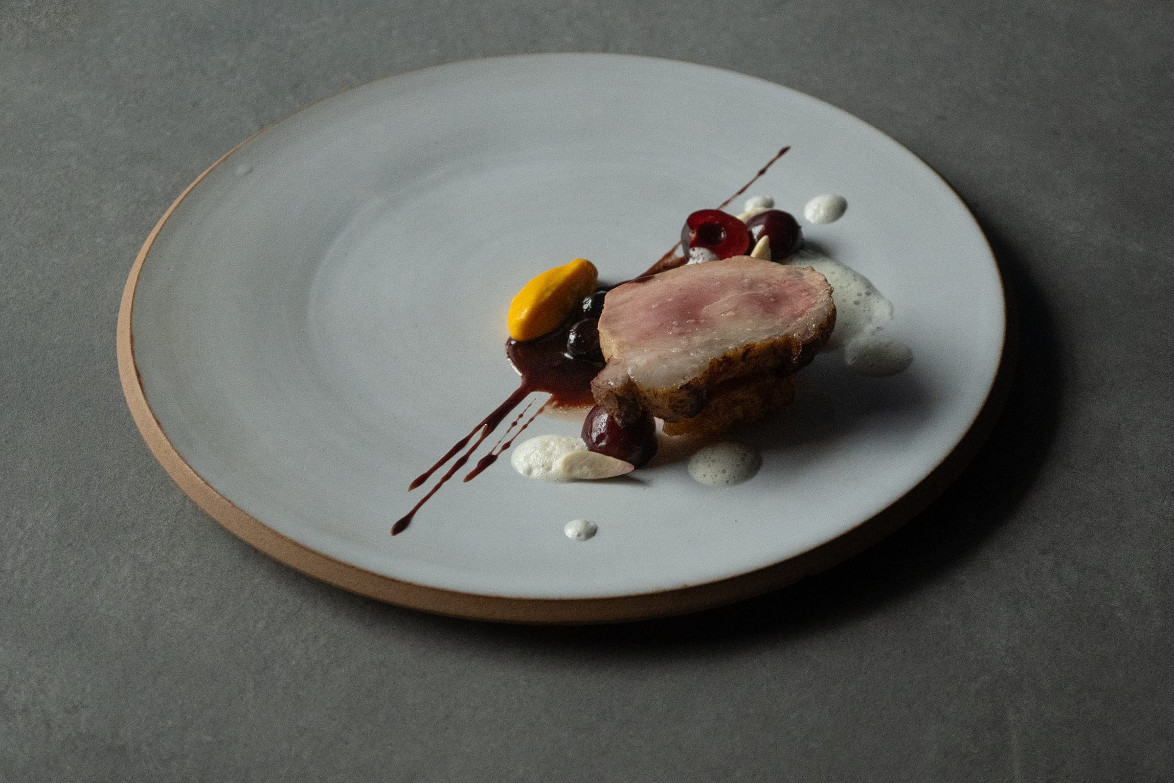 Pink-cooked meat sliced with cherries and chocolate sauce, refined plating on white dish