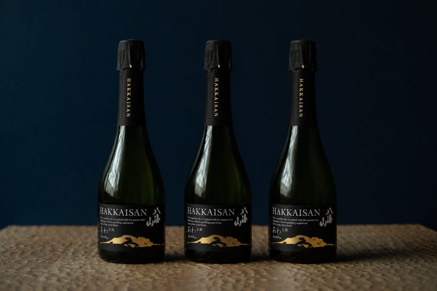 Trois bouteilles de saké pétillant Hakkaisan, étiquette noire et or, fond bleu nuit